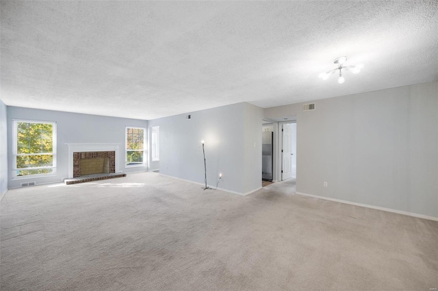 unfurnished living room featuring a fireplace, light colored carpet, a notable chandelier, and a textured ceiling