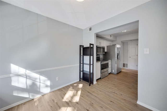 kitchen with a textured ceiling, appliances with stainless steel finishes, and light hardwood / wood-style floors