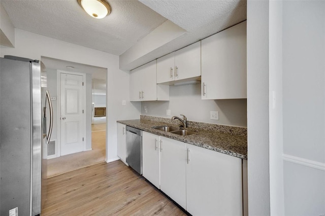 kitchen with white cabinets, stainless steel appliances, a textured ceiling, and light hardwood / wood-style flooring