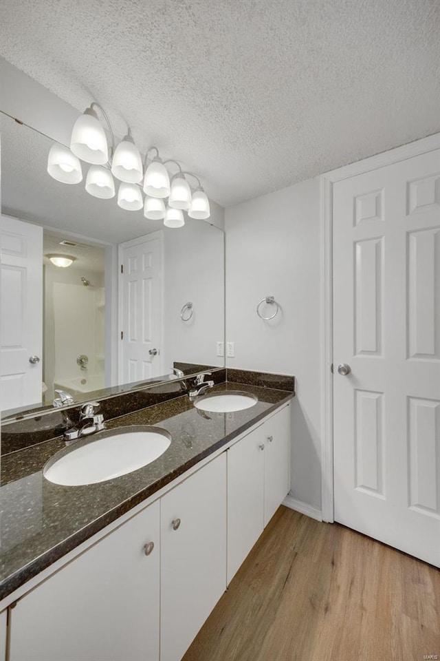 bathroom featuring plus walk in shower, vanity, wood-type flooring, and a textured ceiling