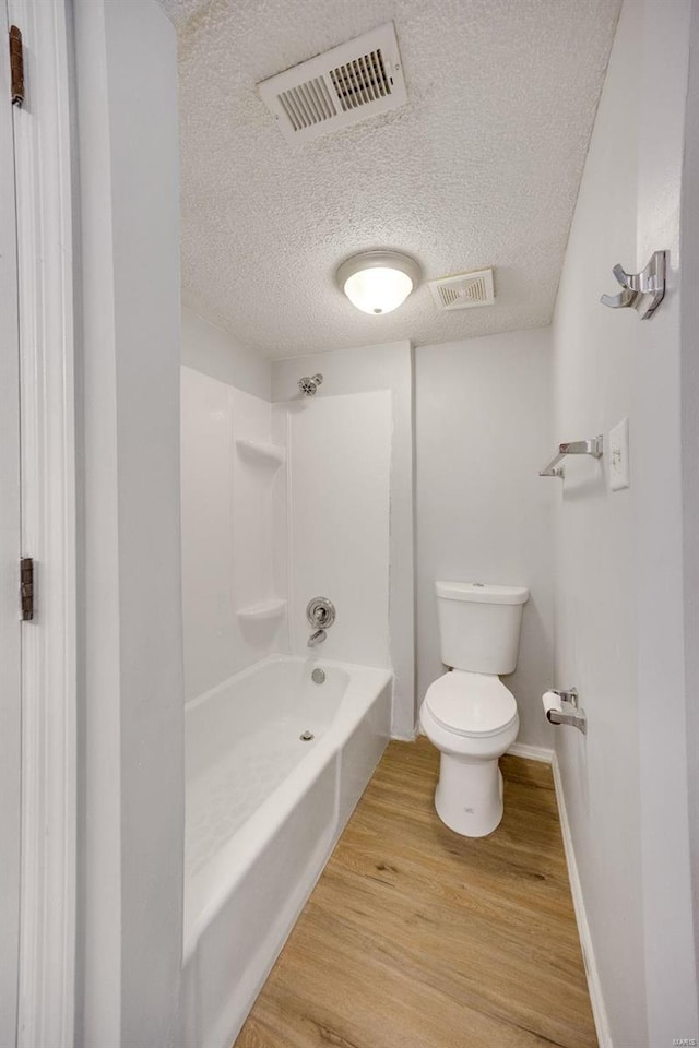 bathroom with toilet, bathtub / shower combination, hardwood / wood-style floors, and a textured ceiling