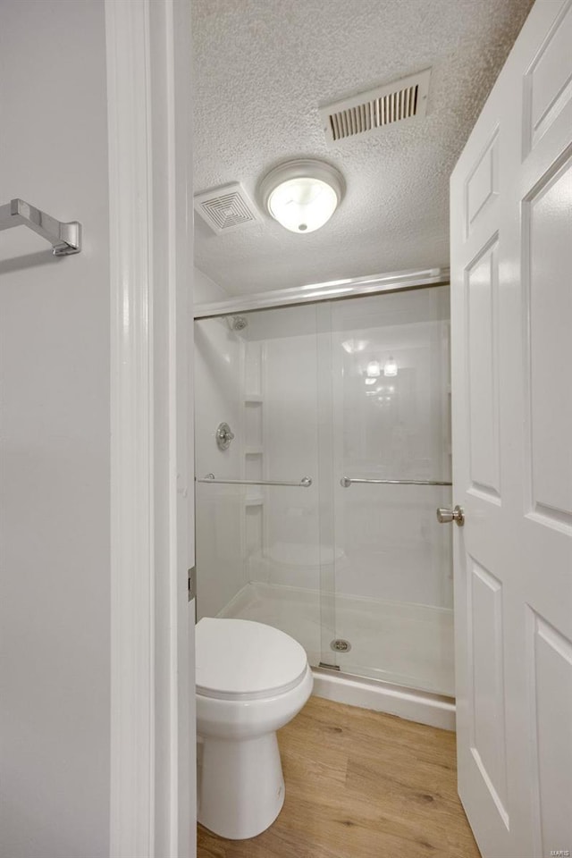 bathroom featuring hardwood / wood-style floors, walk in shower, a textured ceiling, and toilet