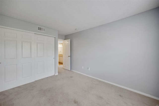 unfurnished bedroom with a closet, a textured ceiling, and light carpet