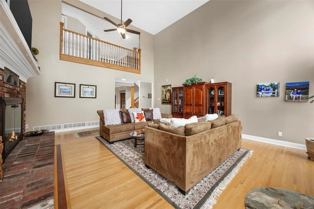 living room with wood-type flooring, high vaulted ceiling, a brick fireplace, and ceiling fan