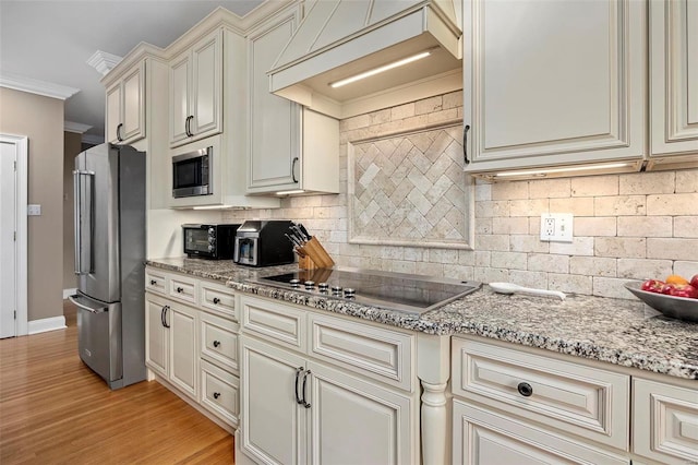 kitchen featuring custom exhaust hood, light hardwood / wood-style flooring, ornamental molding, cream cabinetry, and stainless steel appliances