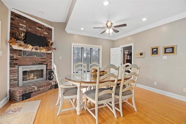 dining room featuring ceiling fan, light hardwood / wood-style floors, crown molding, and a brick fireplace