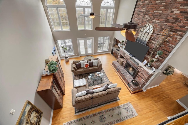 living room featuring a high ceiling, a brick fireplace, ceiling fan, and wood-type flooring