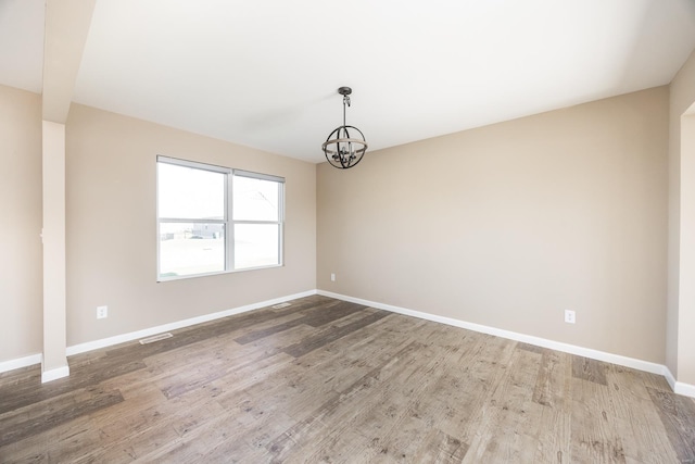 unfurnished room featuring an inviting chandelier, visible vents, baseboards, and wood finished floors