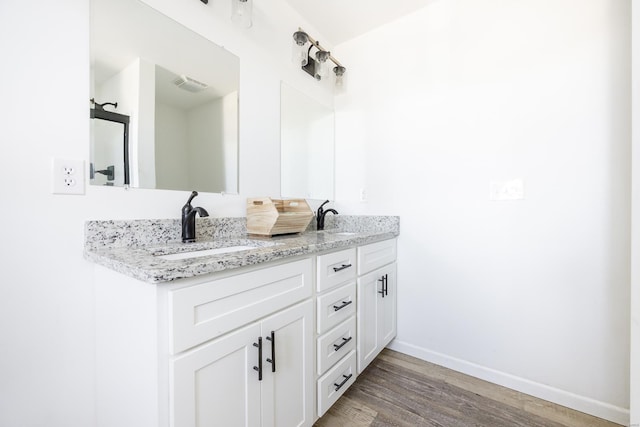 full bathroom with double vanity, baseboards, visible vents, wood finished floors, and a sink