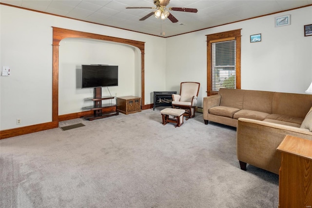 carpeted living room with crown molding, a wood stove, and ceiling fan