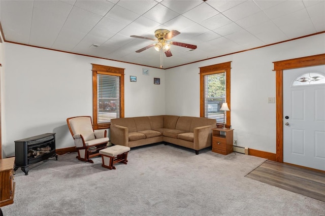 carpeted living room with a wood stove, ornamental molding, baseboard heating, and ceiling fan