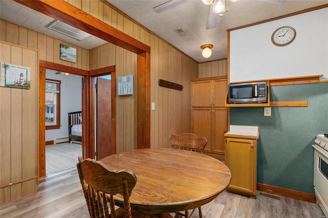 dining area featuring crown molding, wood walls, light hardwood / wood-style flooring, and ceiling fan