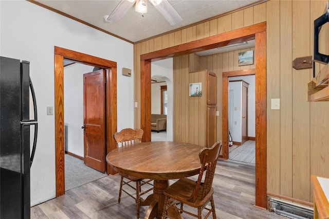 dining area featuring ornamental molding, wood walls, light wood-type flooring, and ceiling fan