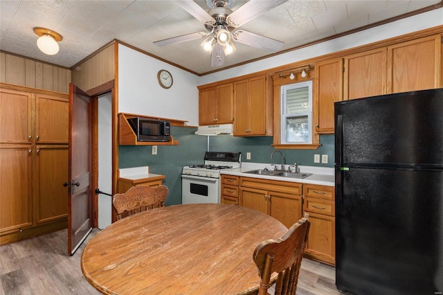 kitchen with white gas range, black refrigerator, ornamental molding, sink, and light wood-type flooring