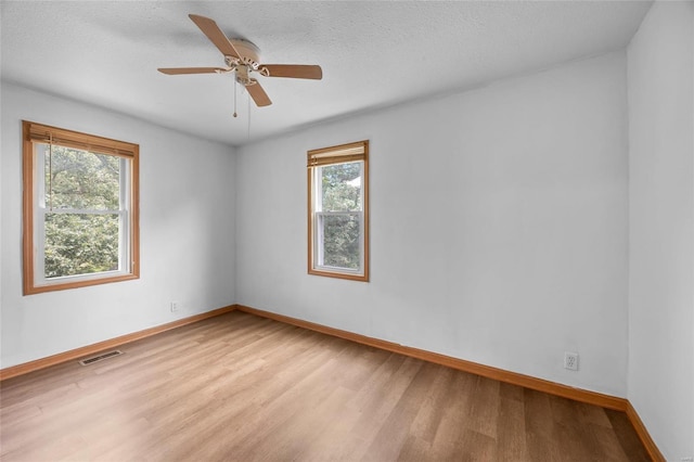 empty room featuring ceiling fan, a healthy amount of sunlight, a textured ceiling, and light hardwood / wood-style floors