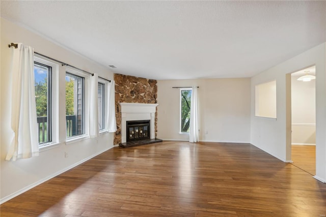 unfurnished living room with wood-type flooring and a stone fireplace