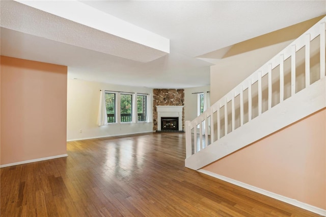 unfurnished living room with a stone fireplace, a textured ceiling, and hardwood / wood-style flooring