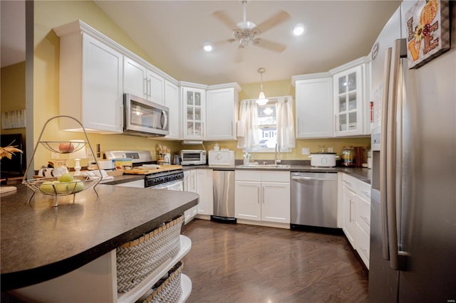 kitchen featuring appliances with stainless steel finishes, white cabinetry, dark wood-type flooring, pendant lighting, and sink