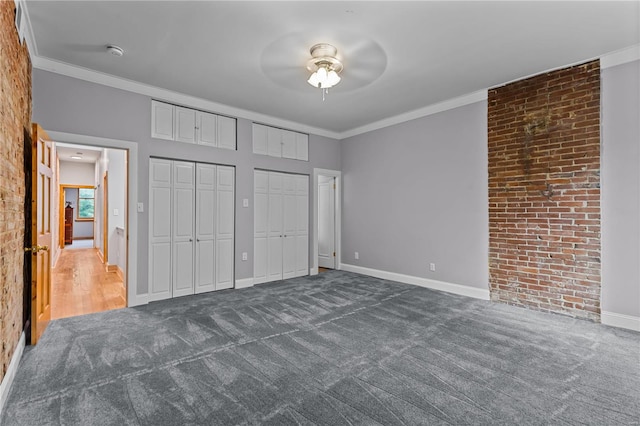 unfurnished bedroom featuring multiple closets, dark carpet, ceiling fan, and crown molding