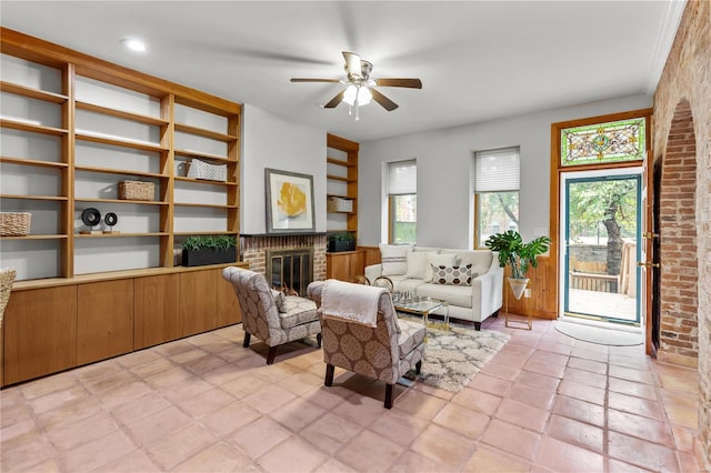 living room featuring ceiling fan, light tile patterned floors, brick wall, and a brick fireplace