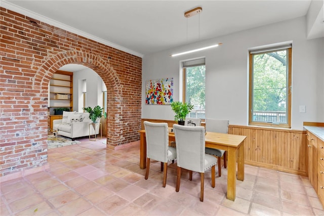 tiled dining room with wood walls, crown molding, and brick wall