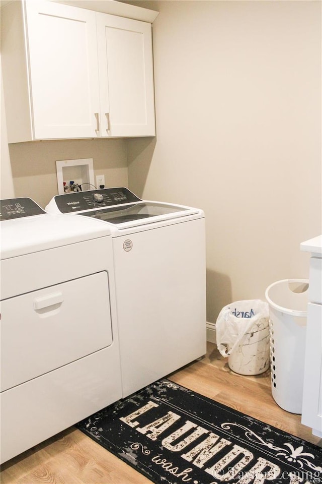 laundry room with light hardwood / wood-style flooring, independent washer and dryer, and cabinets