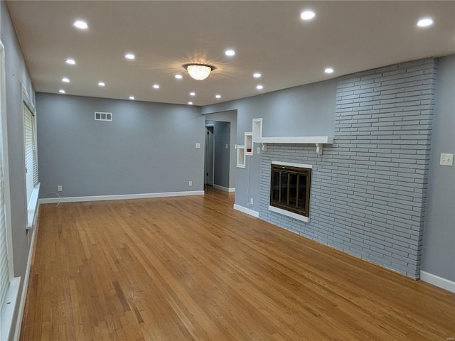 unfurnished living room with a brick fireplace and light wood-type flooring