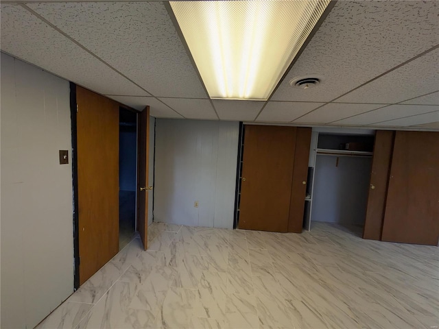 basement featuring a paneled ceiling and wooden walls