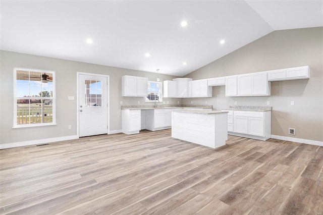 kitchen featuring light stone countertops, light wood-type flooring, a kitchen island, lofted ceiling, and white cabinets