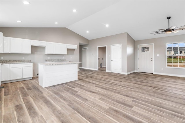 kitchen featuring white cabinetry, light stone countertops, lofted ceiling, and light wood-type flooring