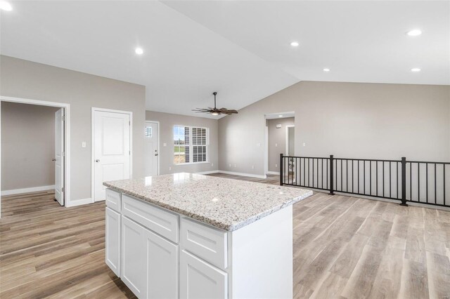 kitchen featuring lofted ceiling, white cabinets, ceiling fan, light wood-type flooring, and light stone counters