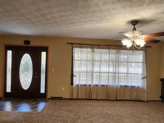 foyer entrance with a textured ceiling, a healthy amount of sunlight, dark carpet, and ceiling fan