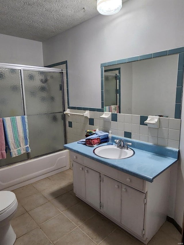 full bathroom with bath / shower combo with glass door, a textured ceiling, toilet, vanity, and tile patterned floors