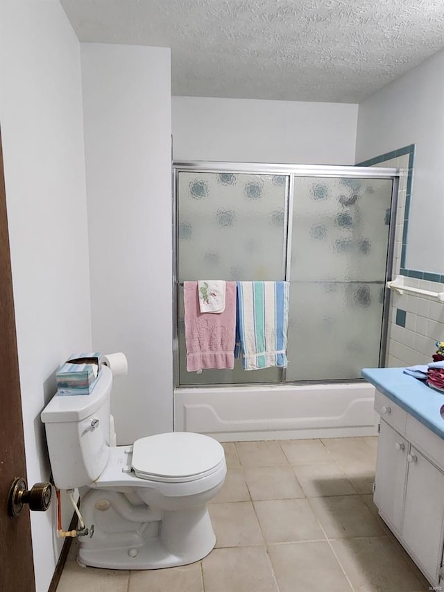 full bathroom featuring a textured ceiling, shower / bath combination with glass door, toilet, vanity, and tile patterned flooring