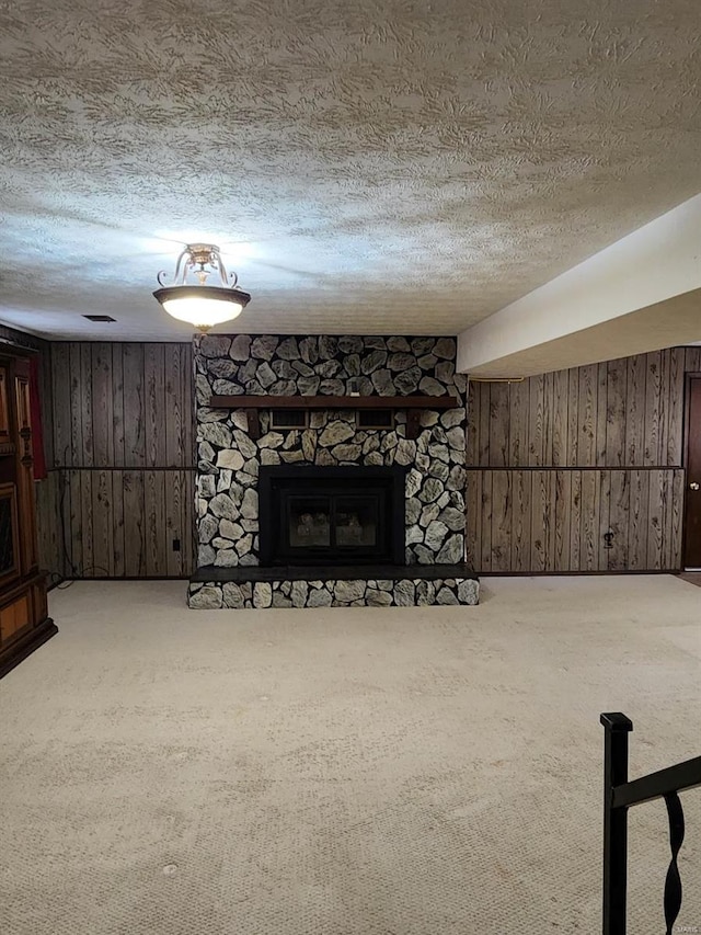 living room with wood walls, a textured ceiling, a fireplace, and carpet floors