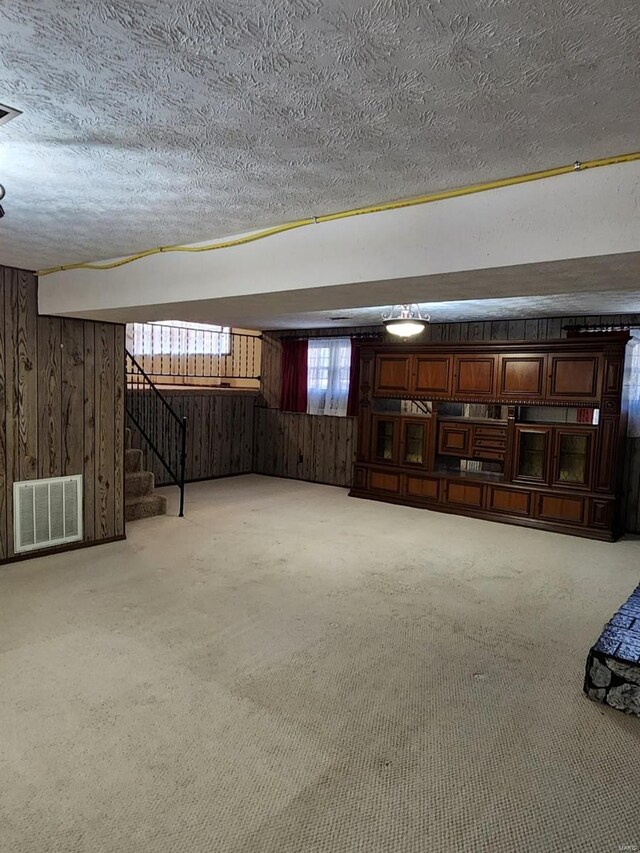 basement with a textured ceiling, light colored carpet, and wood walls