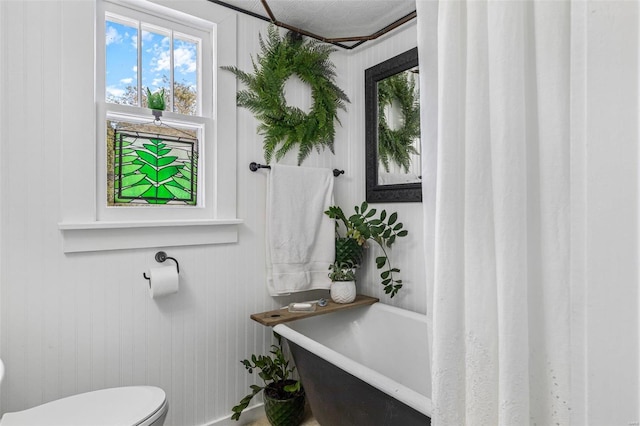 bathroom featuring wood walls, toilet, and a washtub