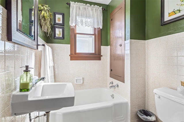 bathroom with toilet, a washtub, sink, and tile walls