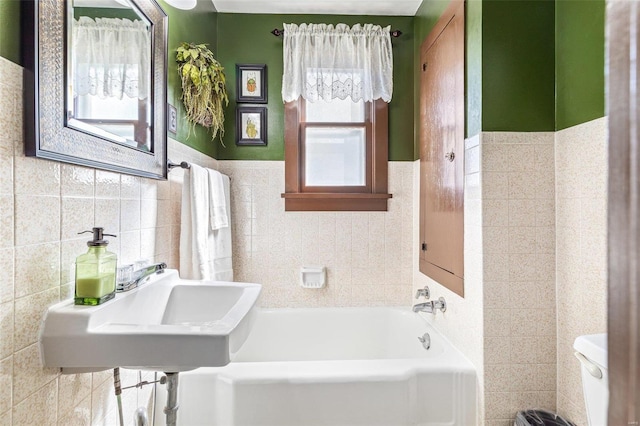 bathroom featuring a bath, toilet, tile walls, and plenty of natural light