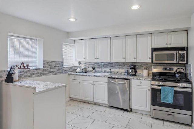 kitchen with kitchen peninsula, stainless steel appliances, backsplash, sink, and white cabinets