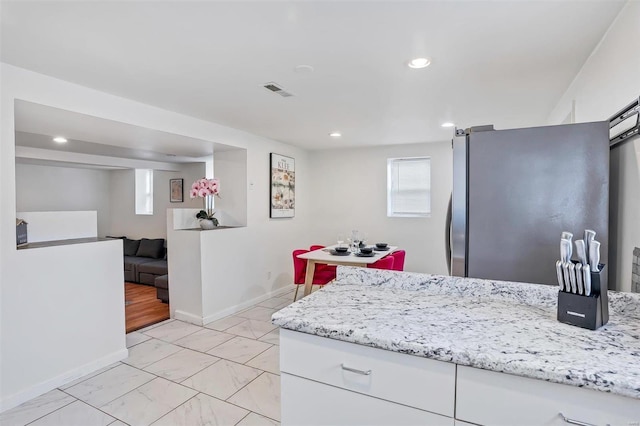 kitchen with light stone countertops, stainless steel fridge, and white cabinets