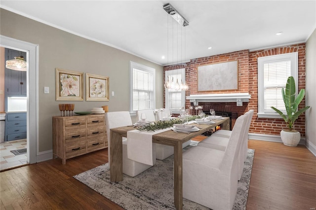 dining room featuring ornamental molding, brick wall, a fireplace, and dark hardwood / wood-style flooring