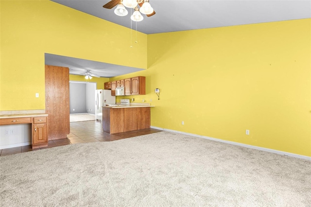 kitchen featuring kitchen peninsula, white appliances, light colored carpet, a towering ceiling, and ceiling fan