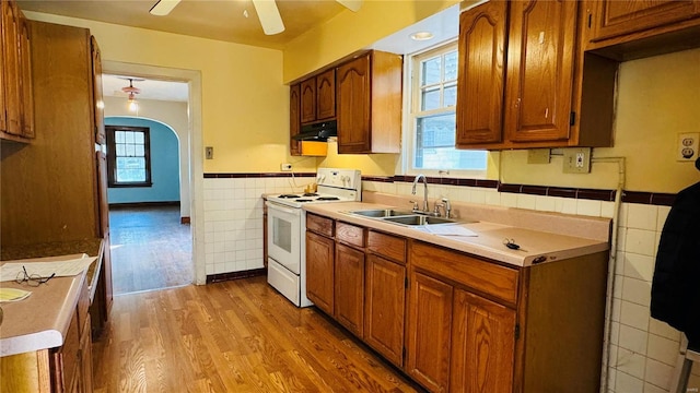 kitchen featuring sink, light wood-type flooring, white electric stove, ceiling fan, and tile walls