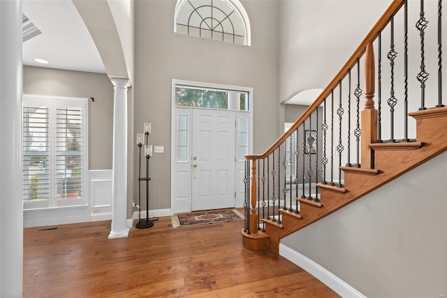 foyer entrance with decorative columns, hardwood / wood-style flooring, and a high ceiling