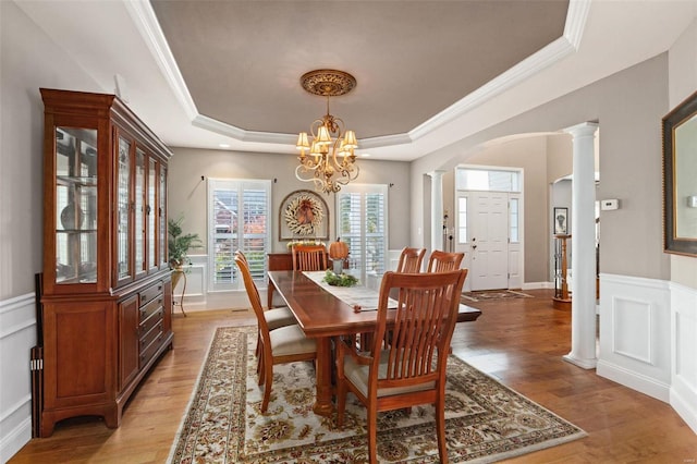 dining space with light wood-type flooring, decorative columns, a tray ceiling, crown molding, and a chandelier