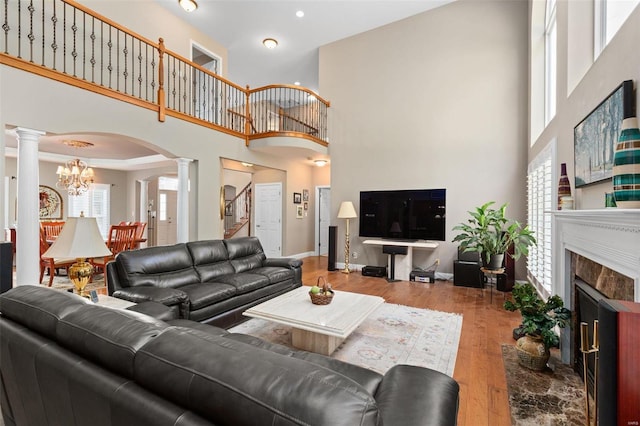 living room with decorative columns, a towering ceiling, wood-type flooring, and a chandelier