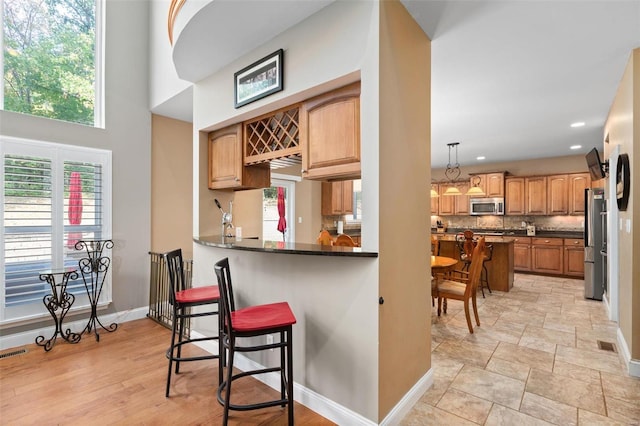 kitchen featuring tasteful backsplash, appliances with stainless steel finishes, kitchen peninsula, a kitchen breakfast bar, and decorative light fixtures