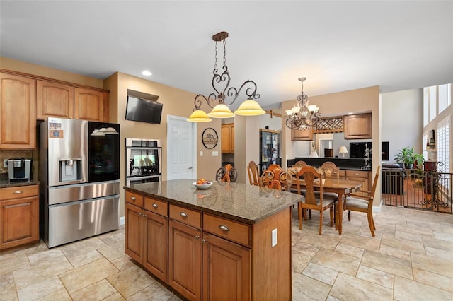 kitchen featuring appliances with stainless steel finishes, a kitchen island, hanging light fixtures, dark stone counters, and an inviting chandelier