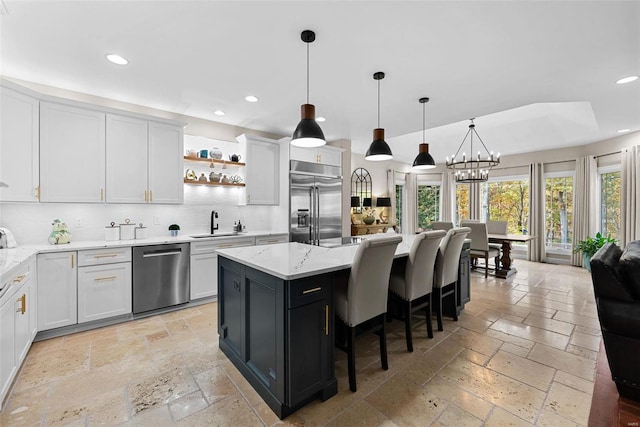 kitchen featuring tasteful backsplash, hanging light fixtures, a kitchen island, white cabinetry, and stainless steel appliances